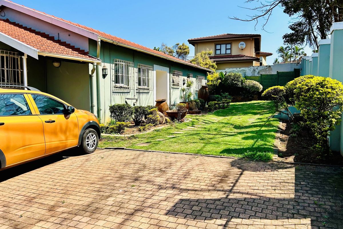 A side view of the property featuring a paved driveway, a well-maintained lawn, and established garden beds alongside the building exterior.