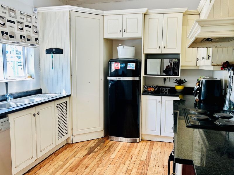 A functional kitchen featuring cream cabinetry, dark granite countertops, a built-in hob, and an integrated extractor fan with timber flooring.