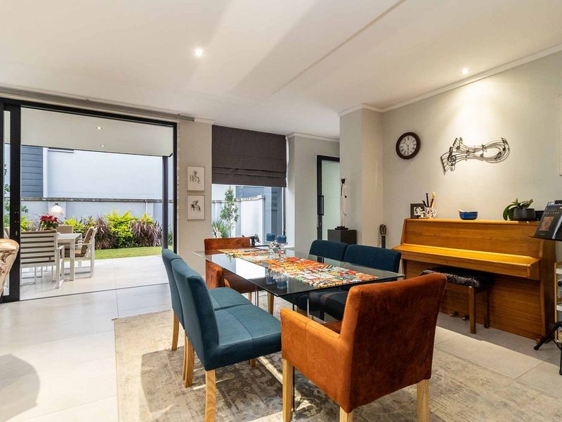 A bright dining area featuring large sliding glass doors that open onto a covered patio and garden, with modern tiled flooring and recessed lighting.