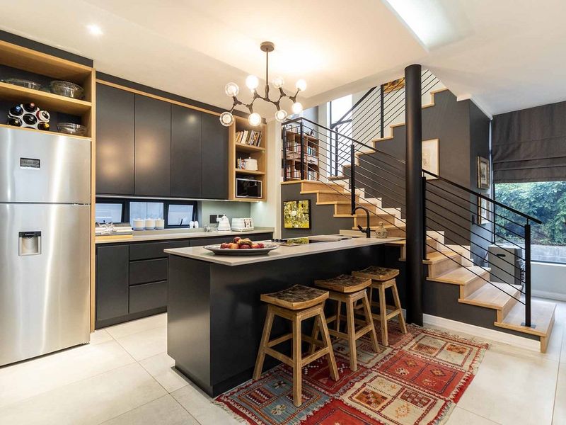 Modern open-plan kitchen featuring sleek dark cabinetry, a central island, and a striking staircase with a metal balustrade, creating a contemporary living space.