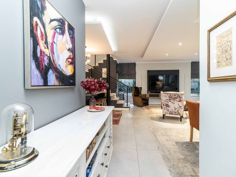 A modern open-plan living area featuring tiled floors, recessed ceiling lighting, and a sleek built-in media wall with an adjacent staircase.