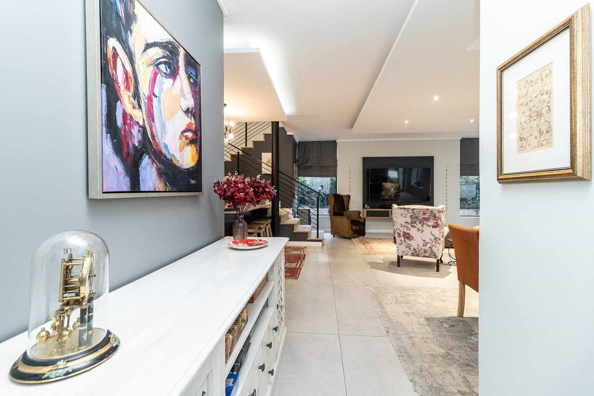 A modern open-plan living area featuring tiled floors, recessed ceiling lighting, and a sleek built-in media wall with an adjacent staircase.