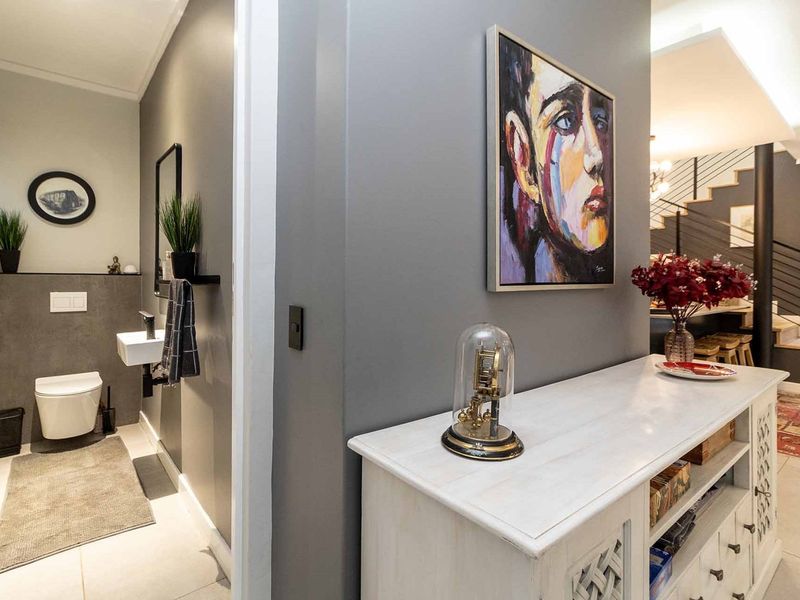 A modern hallway featuring a guest bathroom with a wall-mounted toilet and basin, leading towards a staircase with a contemporary metal railing.
