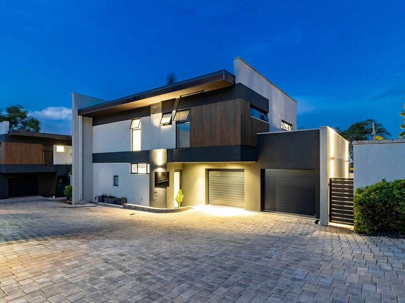 Modern townhouse exterior featuring a paved driveway, double garage, and contemporary architectural finishes with integrated evening lighting.