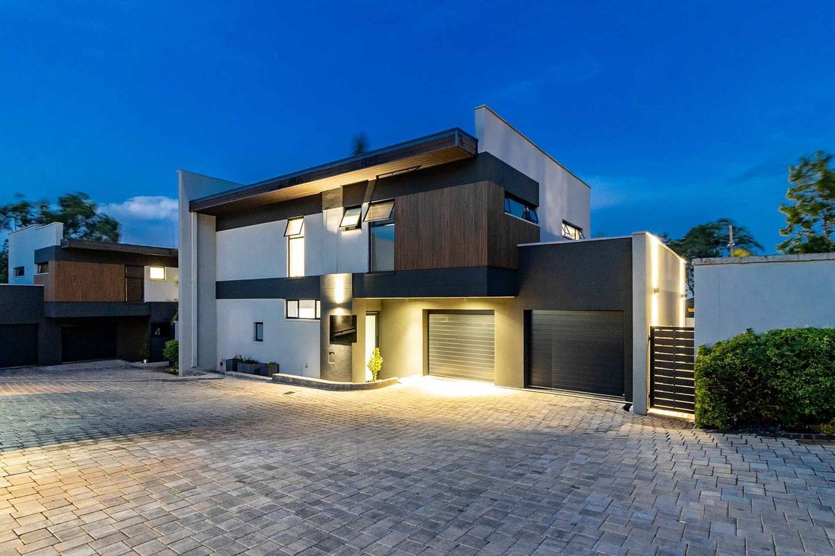 Modern townhouse exterior featuring a paved driveway, double garage, and contemporary architectural finishes with integrated evening lighting.