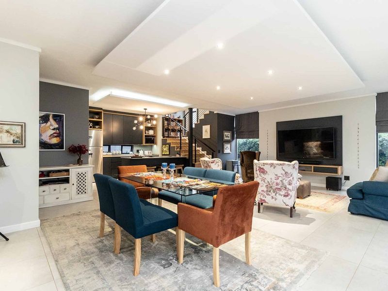 Spacious open-plan living and dining area featuring a modern kitchen, built-in media wall, and a feature staircase with recessed ceiling lighting.