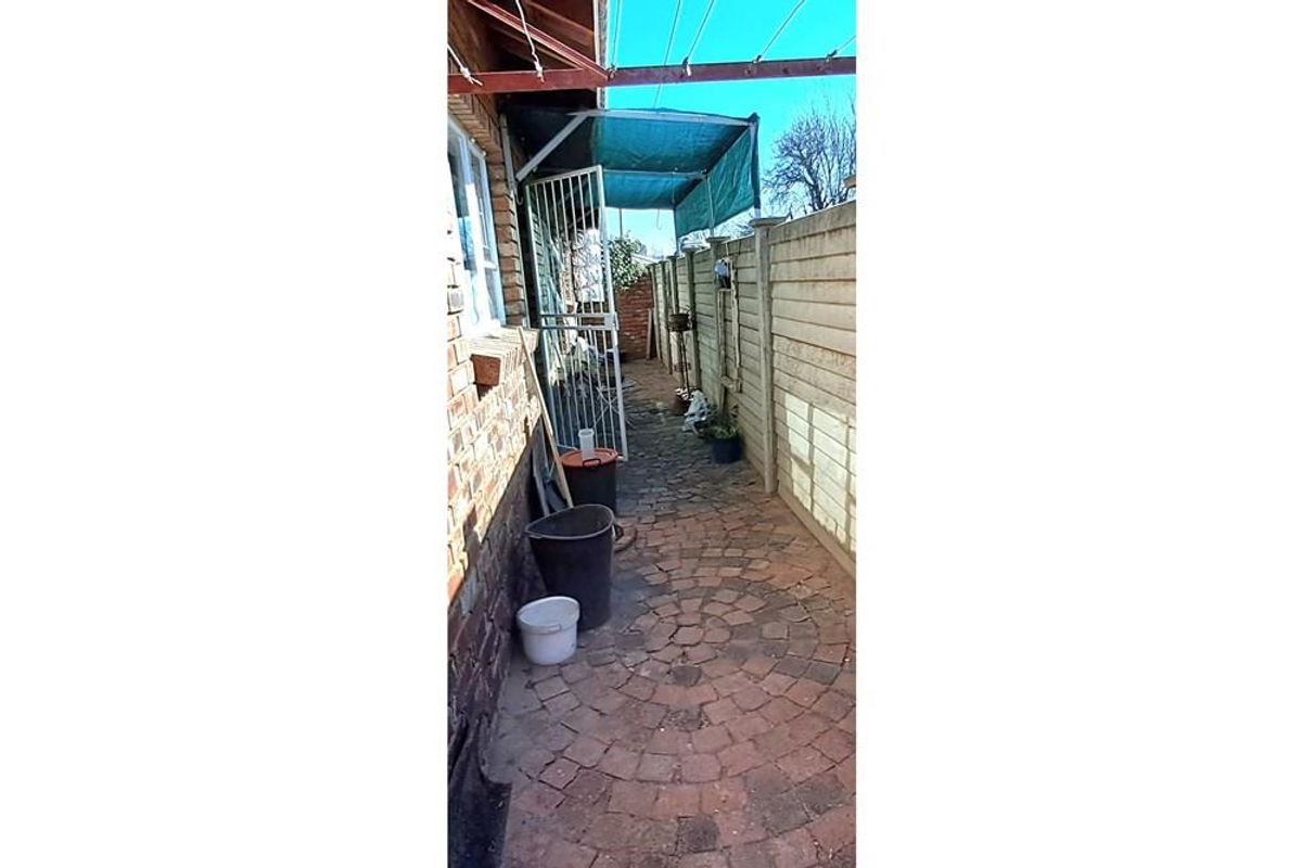 A narrow side exterior area featuring brick paving, a metal security gate, and a basic shade cloth structure along the boundary wall.