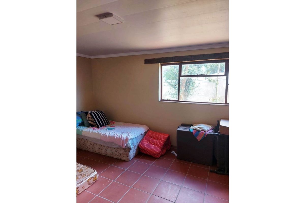 A simple bedroom featuring terracotta floor tiles, a single window with a timber lintel, and a basic ceiling light fixture.