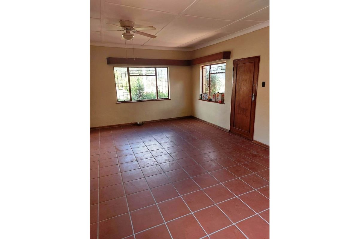 A spacious living room featuring terracotta floor tiles, a ceiling fan, and wooden door frames, offering a blank canvas for interior design.
