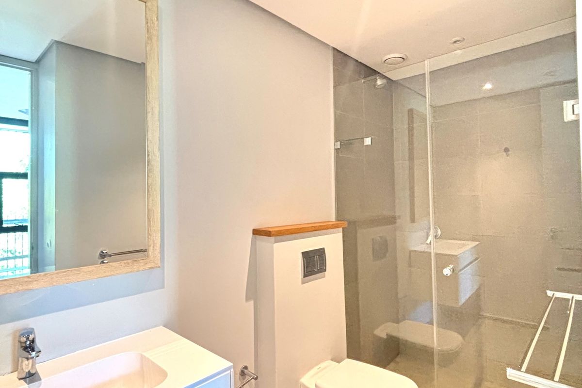 Modern bathroom featuring a glass-enclosed shower, wall-mounted toilet with concealed cistern, and a vanity with a framed mirror.