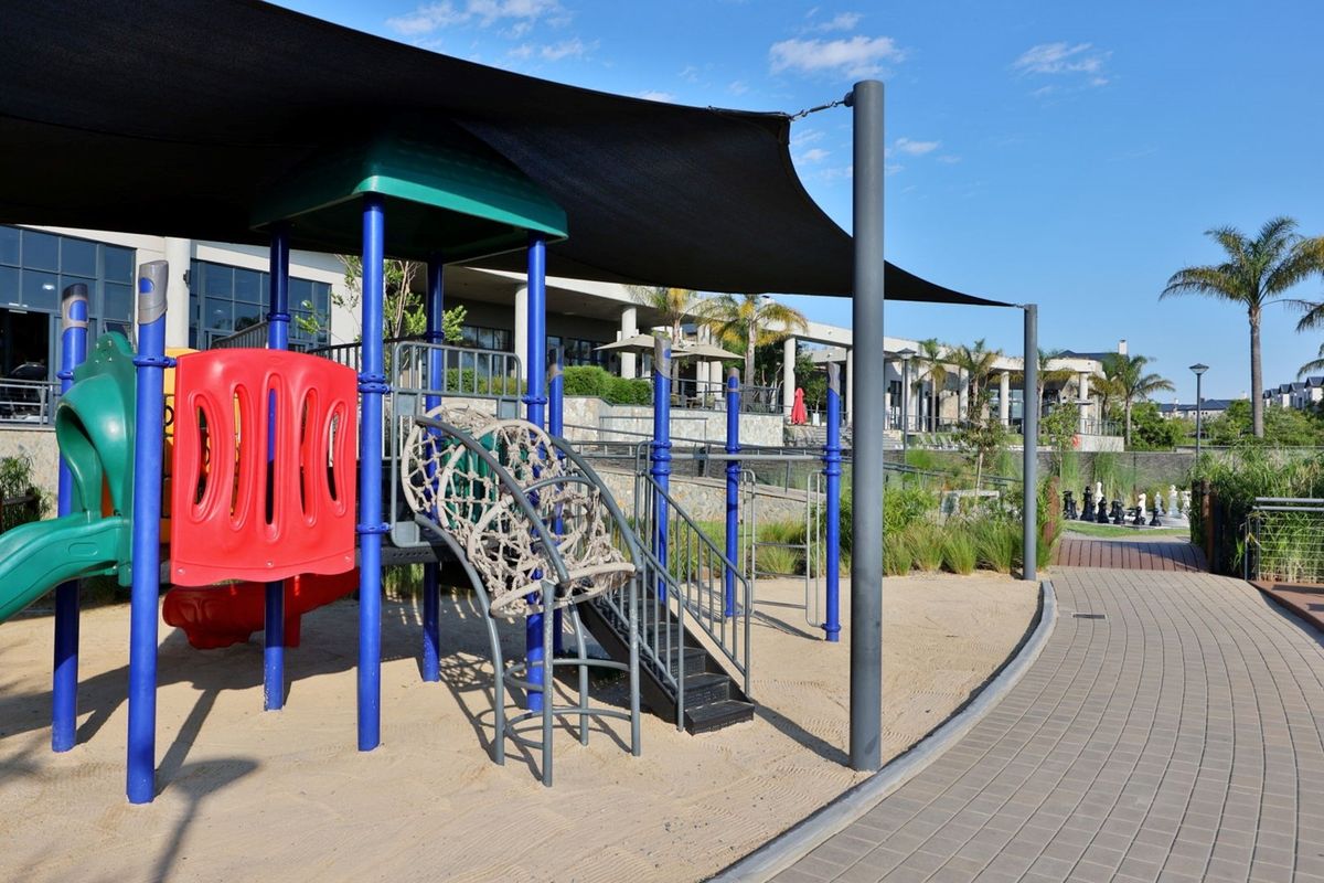 A well-maintained outdoor playground area featuring a shaded jungle gym, sand pit, and paved walkways within the apartment complex grounds.