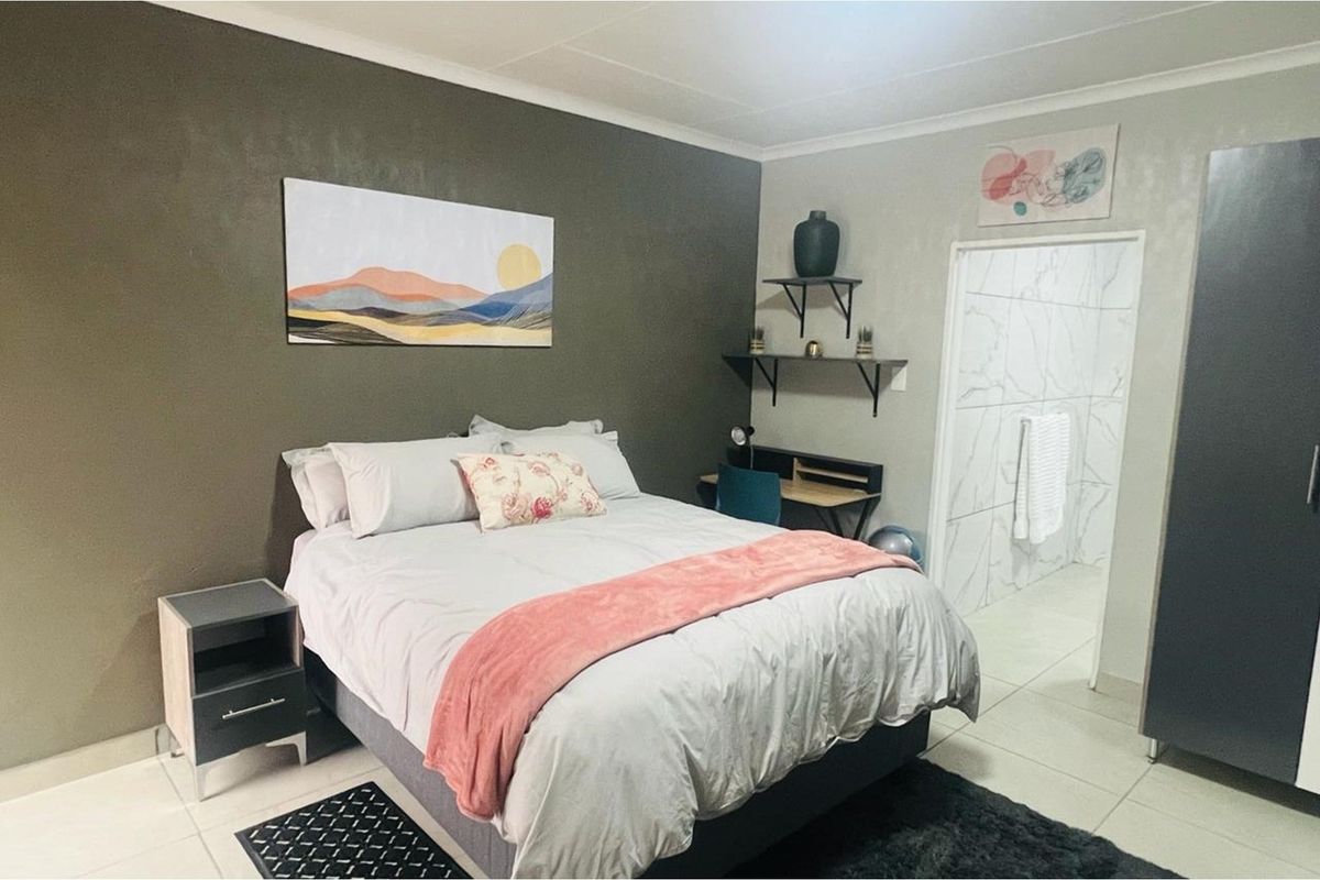 A well-maintained bedroom featuring tiled flooring, a neutral color palette, and an en-suite bathroom with marble-effect wall tiling.