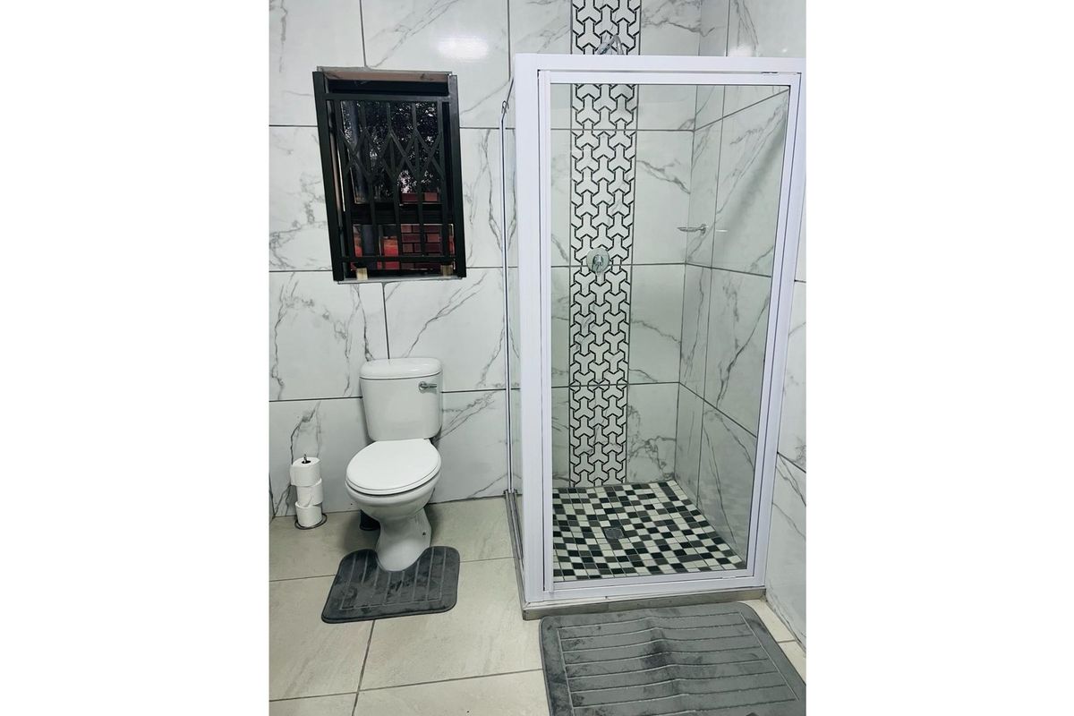 Modern bathroom featuring floor-to-ceiling marble-look wall tiles, a glass-enclosed shower with decorative accent tiling, and a standard toilet.