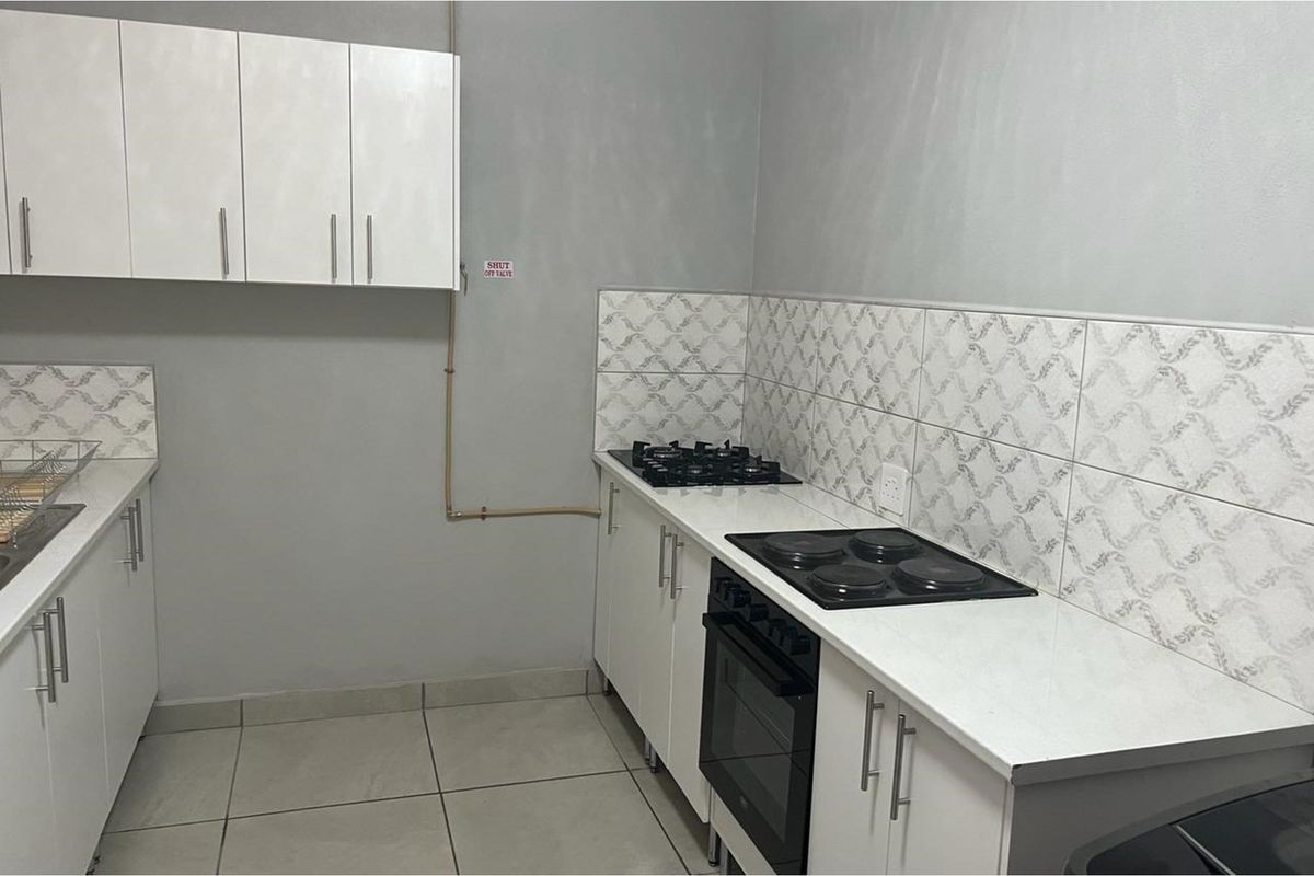 A functional kitchen featuring white cabinetry, tiled splashbacks, a built-in oven, and a combined gas and electric hob setup.