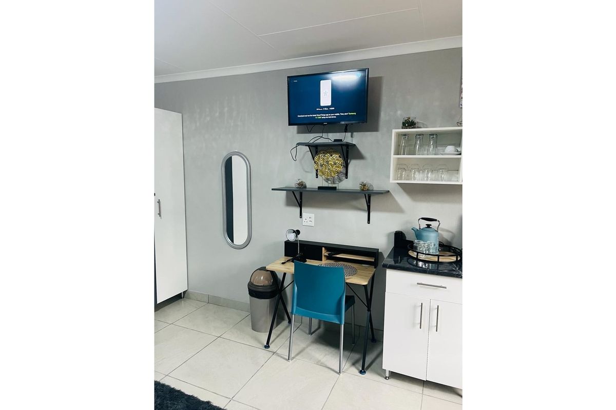 A functional living area featuring tiled flooring, built-in cabinetry, wall-mounted shelving, and a dedicated workspace area.