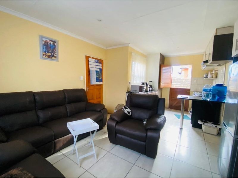Open-plan living area featuring tiled flooring and a compact kitchen with built-in cabinetry and a breakfast counter, leading to an exterior door.