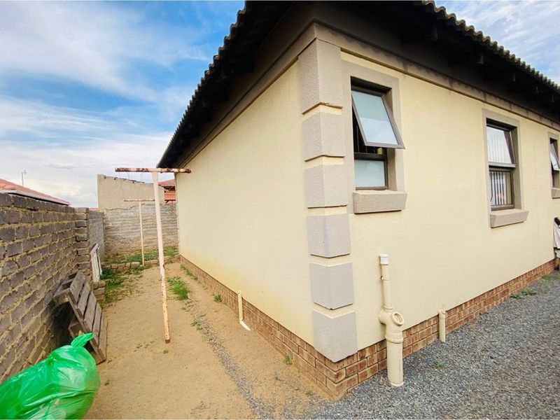 Rear exterior view of the property showing plastered walls, brick plinth, top-hung windows, and a side yard area with a metal washing line.