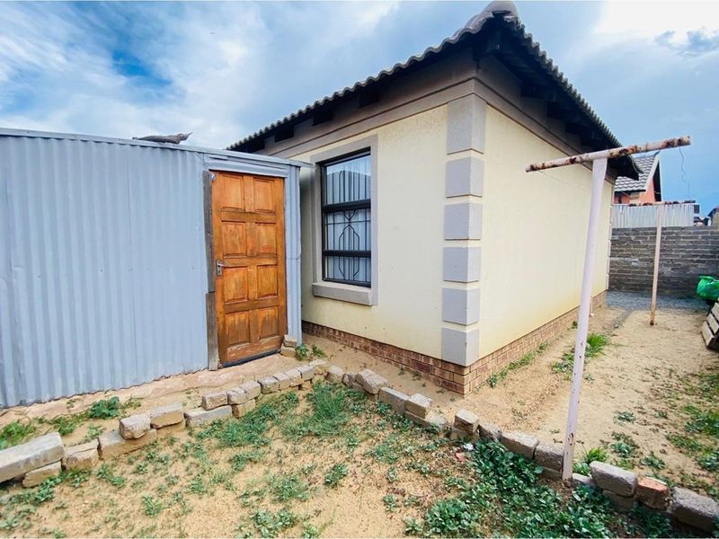 Rear view of the property featuring a corrugated iron utility structure, security-barred window, and a basic outdoor area with brick boundary walling.