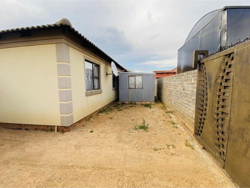 Rear exterior view of the property featuring a concrete block boundary wall, a metal storage shed, and an unpaved yard area.