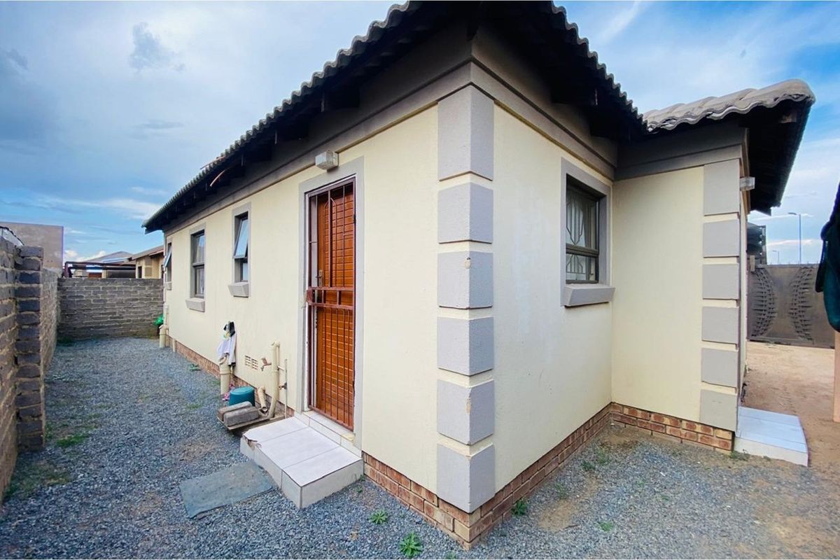 Rear exterior view of the house featuring a security gate, tiled roof, and gravel ground cover.
