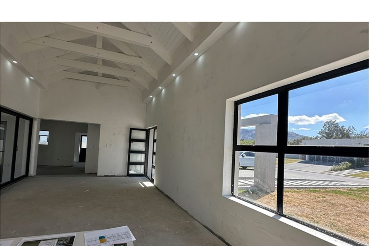 Spacious open-plan living area featuring a high vaulted ceiling with exposed trusses, recessed lighting, and large black-framed windows overlooking the exterior.