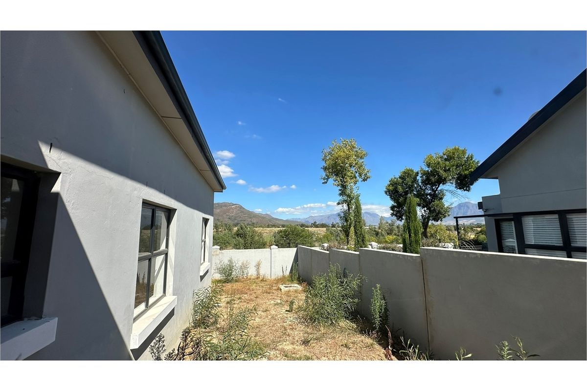Rear exterior view of the property featuring a boundary wall, aluminium window frames, and an unlandscaped garden area with mountain views.