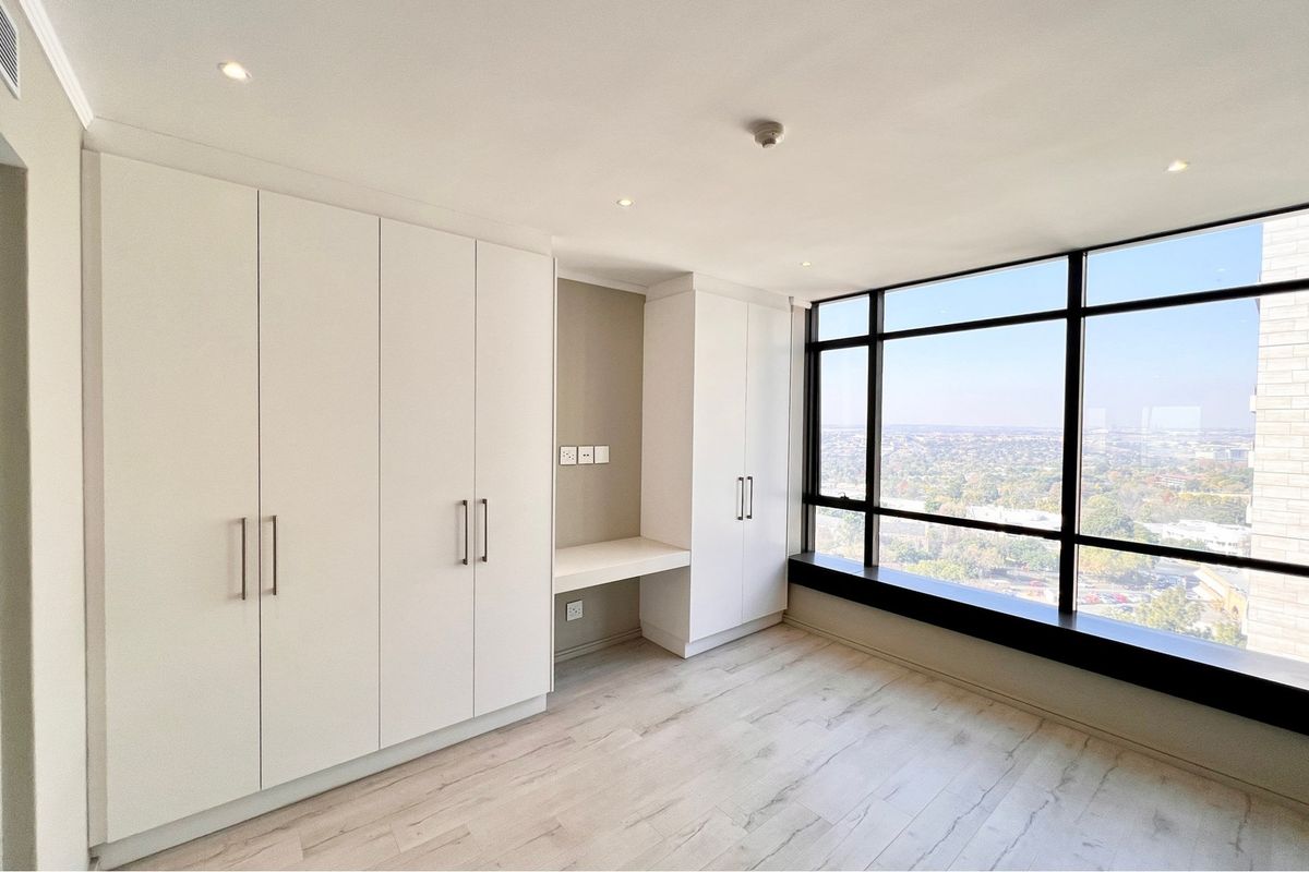 Modern bedroom featuring extensive built-in cabinetry, a dedicated integrated desk area, and expansive floor-to-ceiling windows offering panoramic city views.