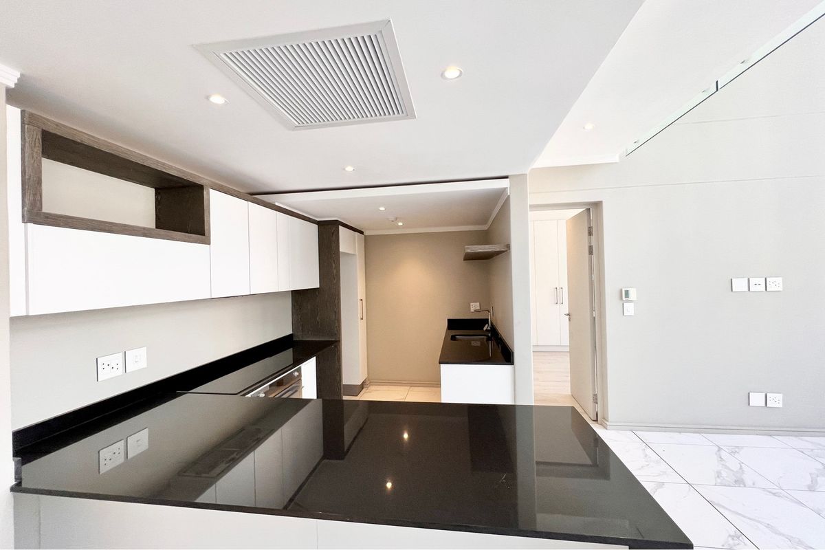 Modern kitchen featuring sleek white and dark wood cabinetry, black granite countertops, integrated appliances, and recessed lighting in a clean, open-plan layout.