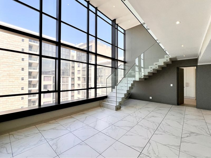 Spacious double-volume living area featuring floor-to-ceiling windows, modern marble-look tiling, and a contemporary floating staircase with glass balustrades.