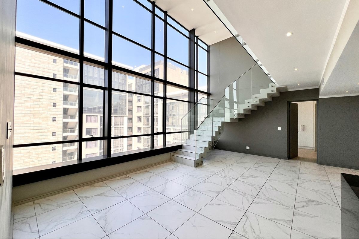 Spacious double-volume living area featuring floor-to-ceiling windows, modern marble-look tiling, and a contemporary floating staircase with glass balustrades.
