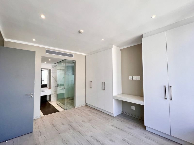 Modern bedroom featuring extensive built-in cabinetry, integrated desk space, light laminate flooring, and direct access to a contemporary en-suite bathroom.
