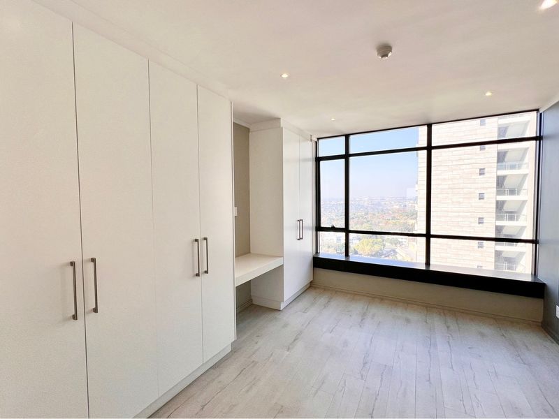 Modern bedroom featuring extensive built-in cabinetry, a integrated desk, light laminate flooring, and expansive windows offering elevated city views.
