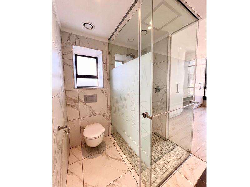 Modern bathroom featuring a spacious walk-in shower with frosted glass, wall-hung toilet with concealed cistern, and elegant marble-look porcelain tiling throughout.