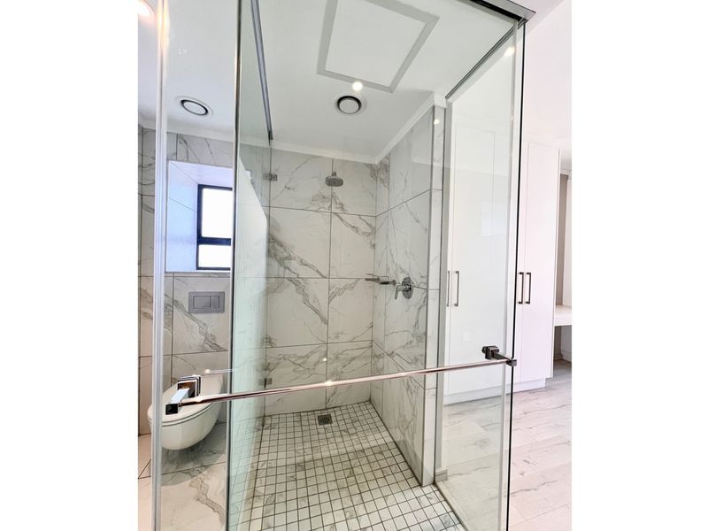 Modern bathroom featuring a glass-enclosed shower with marble-look tiling, a wall-mounted toilet, and sleek built-in cabinetry.