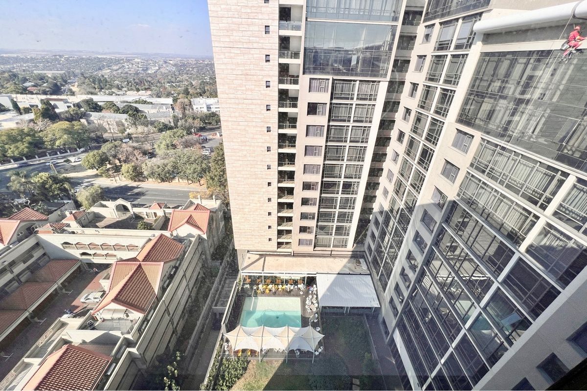 High-angle aerial view of the penthouse building complex, showcasing the architectural facade, surrounding urban landscape, and ground-level pool area.