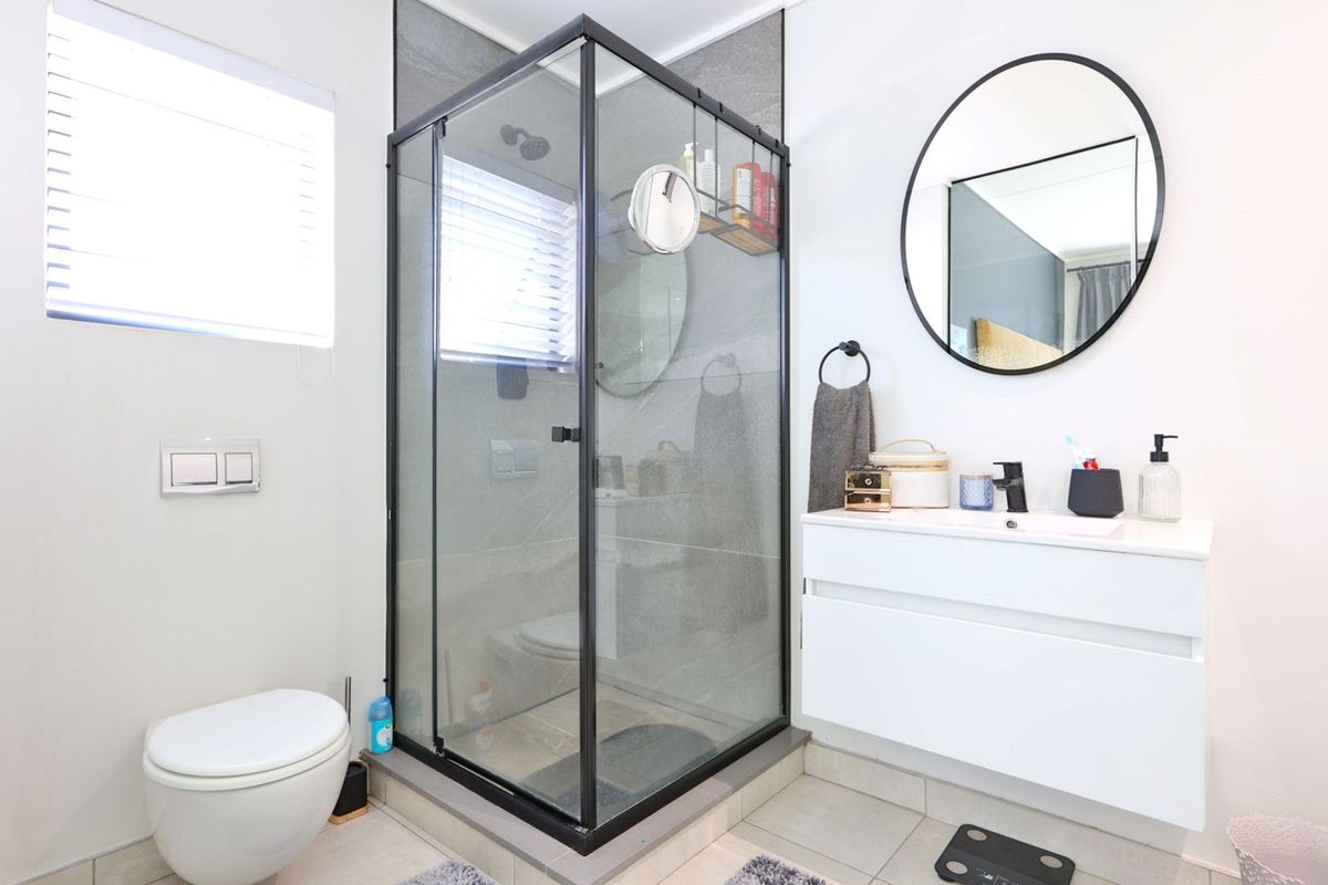Modern bathroom featuring a glass-enclosed shower, wall-mounted toilet, and a sleek white vanity cabinet with a contemporary basin and mirror.