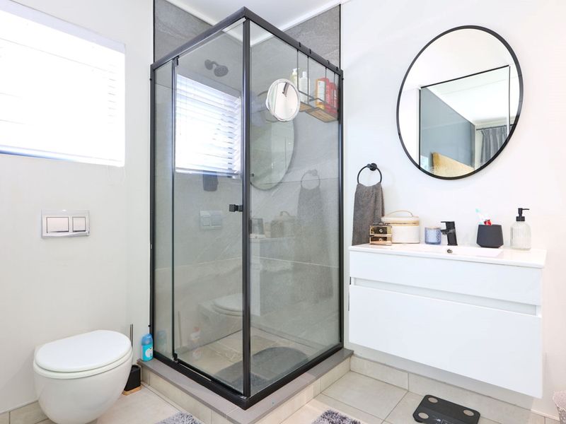 Modern bathroom featuring a glass-enclosed shower, wall-mounted toilet, and a sleek white vanity cabinet with a contemporary basin and mirror.