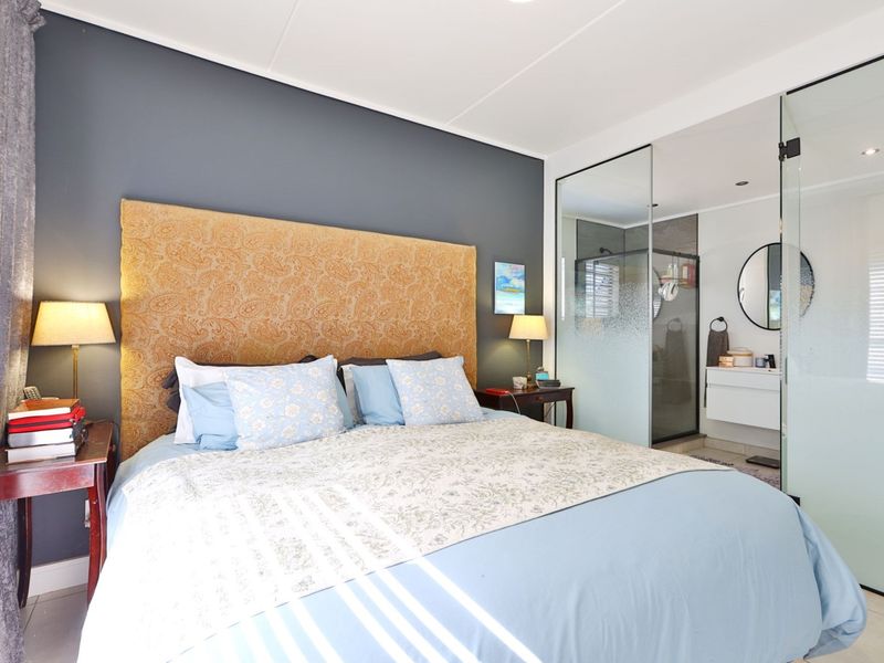 A modern bedroom featuring a dark accent wall and an integrated en-suite bathroom separated by a contemporary glass partition wall.
