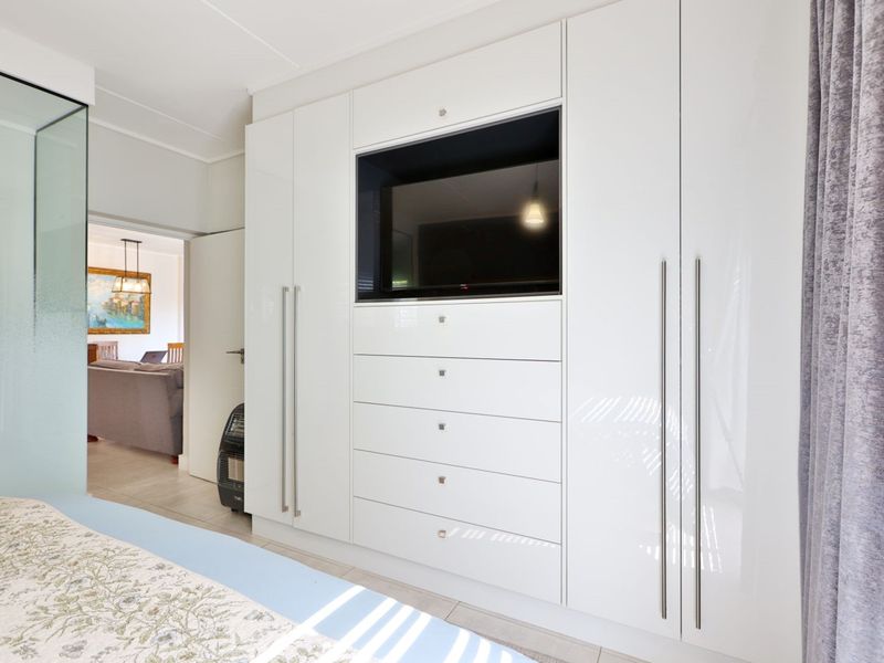 A modern bedroom featuring extensive white high-gloss built-in cabinetry with an integrated television unit and a sleek glass partition.