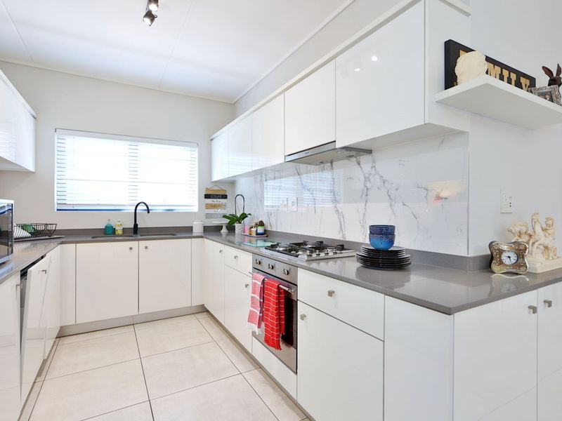Modern kitchen featuring white high-gloss cabinetry, stone countertops, marble-look splashback, and integrated stainless steel appliances.