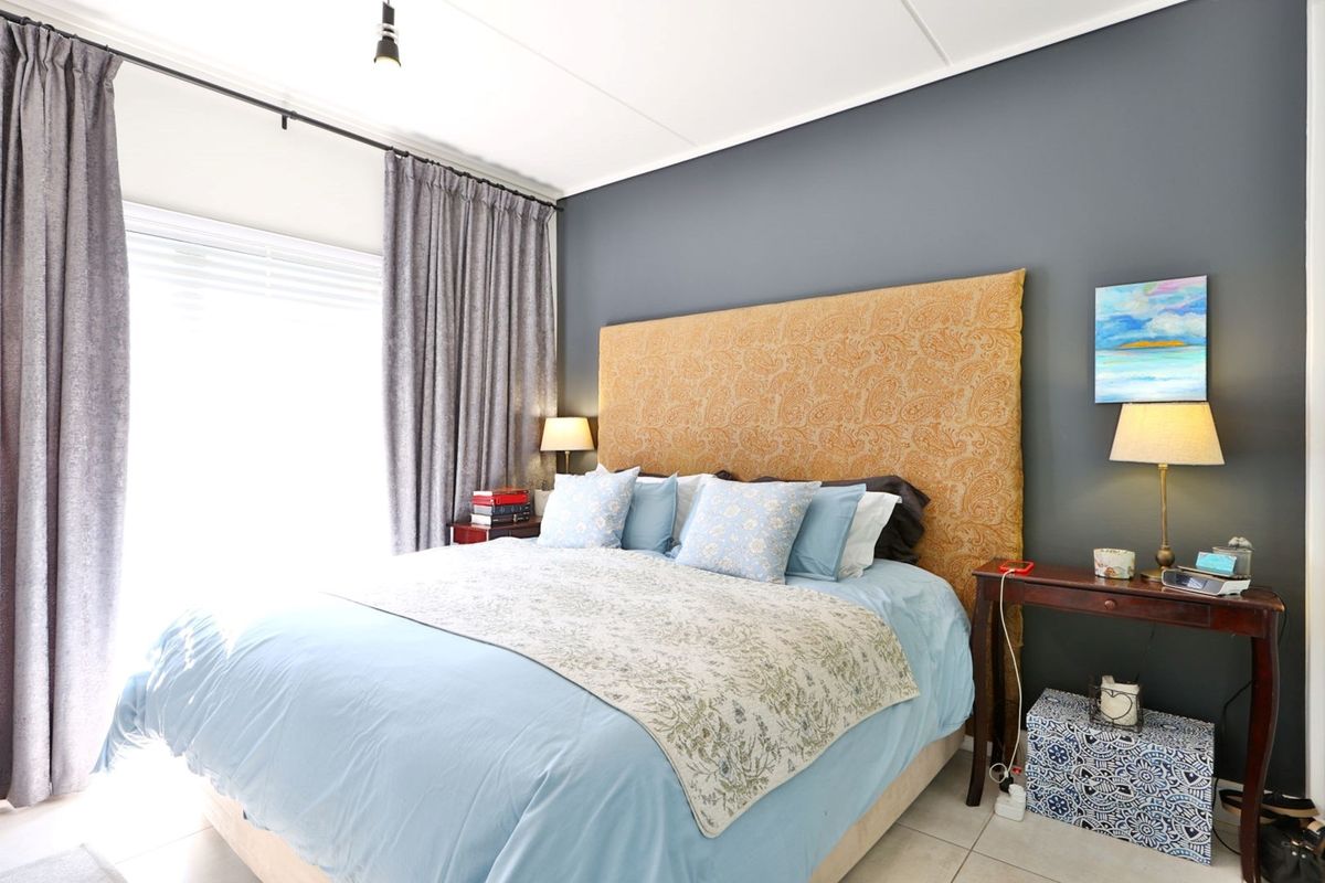 A well-maintained bedroom featuring neutral tiled flooring, a dark accent wall, and large windows with installed curtain tracks.