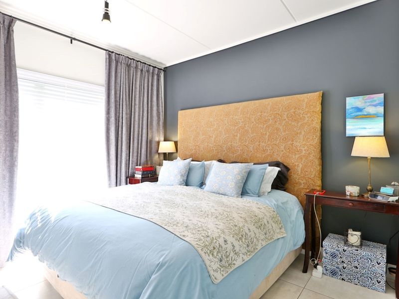 A well-maintained bedroom featuring neutral tiled flooring, a dark accent wall, and large windows with installed curtain tracks.