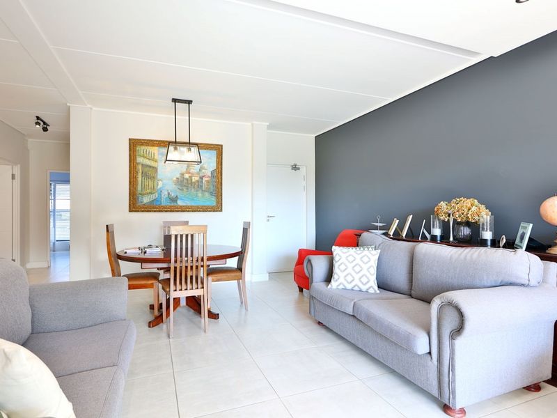 An open-plan living and dining area featuring neutral tiled flooring, a dark grey accent wall, and modern pendant lighting.