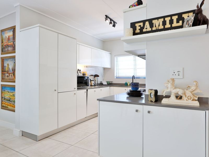Modern kitchen featuring sleek white cabinetry, stone countertops, and tiled flooring, offering a clean and functional workspace.