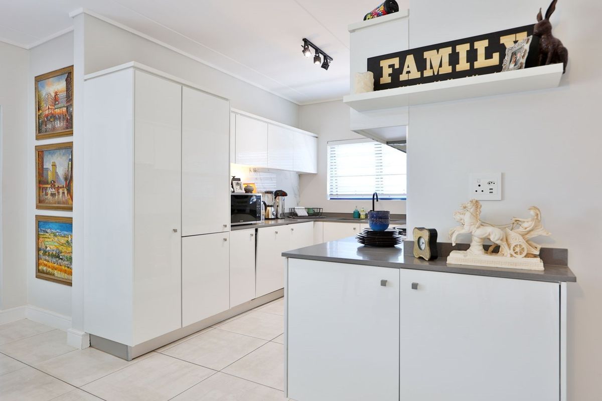 Modern kitchen featuring sleek white cabinetry, stone countertops, and tiled flooring, offering a clean and functional workspace.