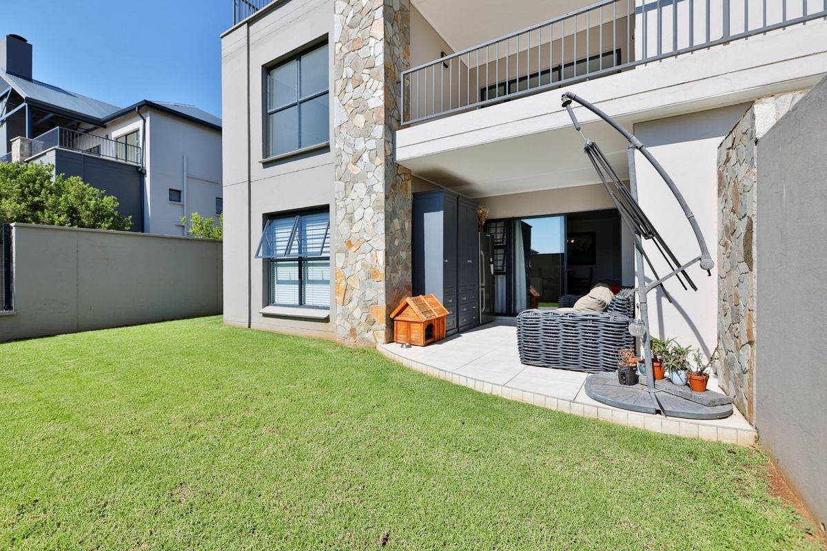 Rear view of the apartment featuring a private garden, tiled patio area, stone-clad facade, and an upper-level balcony with metal railings.