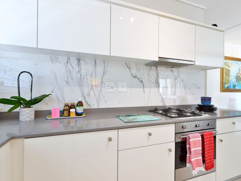 Modern kitchen featuring white gloss cabinetry, a marble-look splashback, stone countertops, and integrated stainless steel appliances including a gas cooktop and oven.