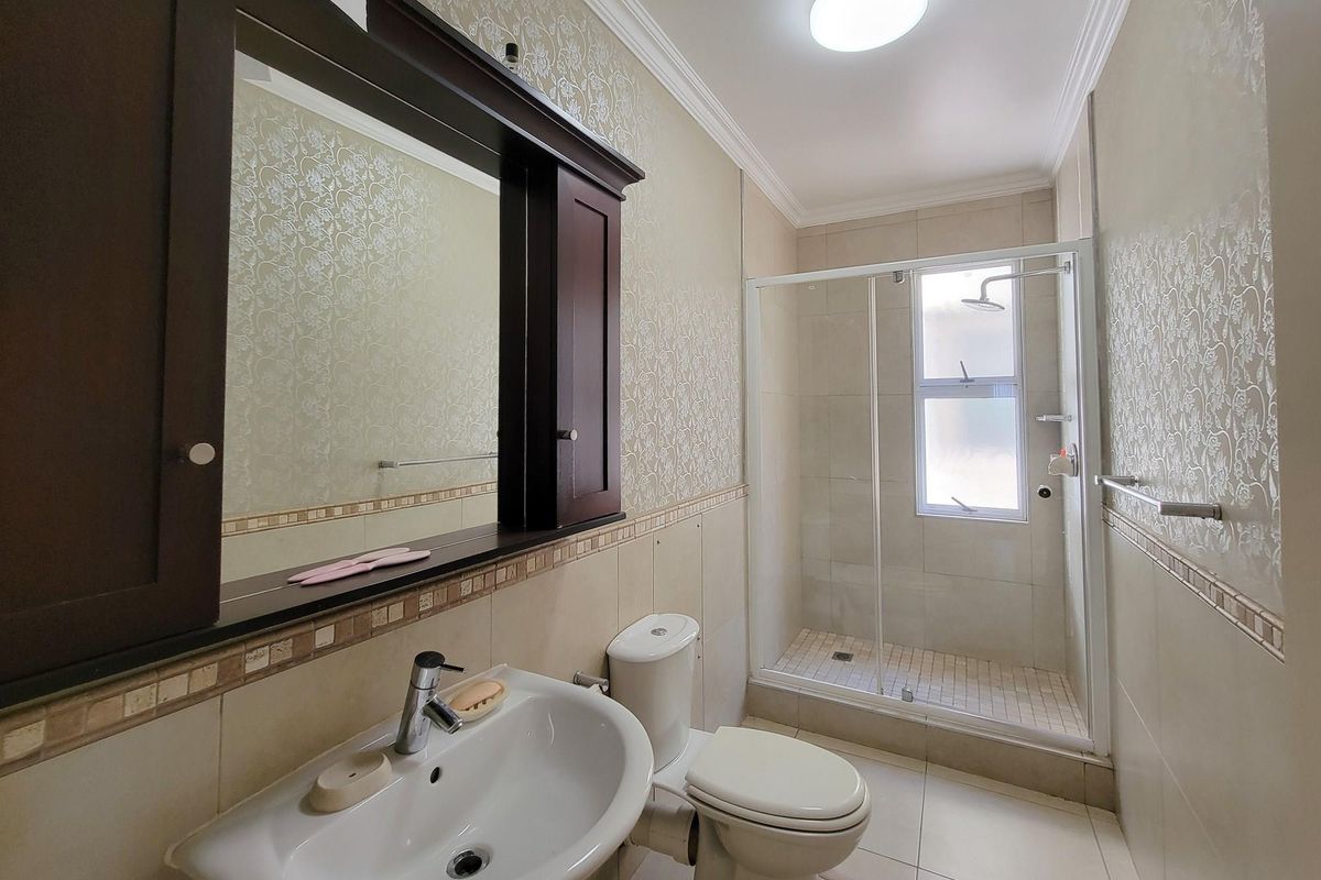 A functional bathroom featuring a glass-enclosed shower, pedestal basin, toilet, and decorative wallpaper finish.