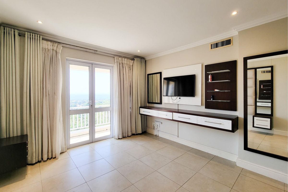 A bright living room featuring tiled flooring, a built-in media console with shelving, and glass sliding doors leading to a balcony with scenic views.