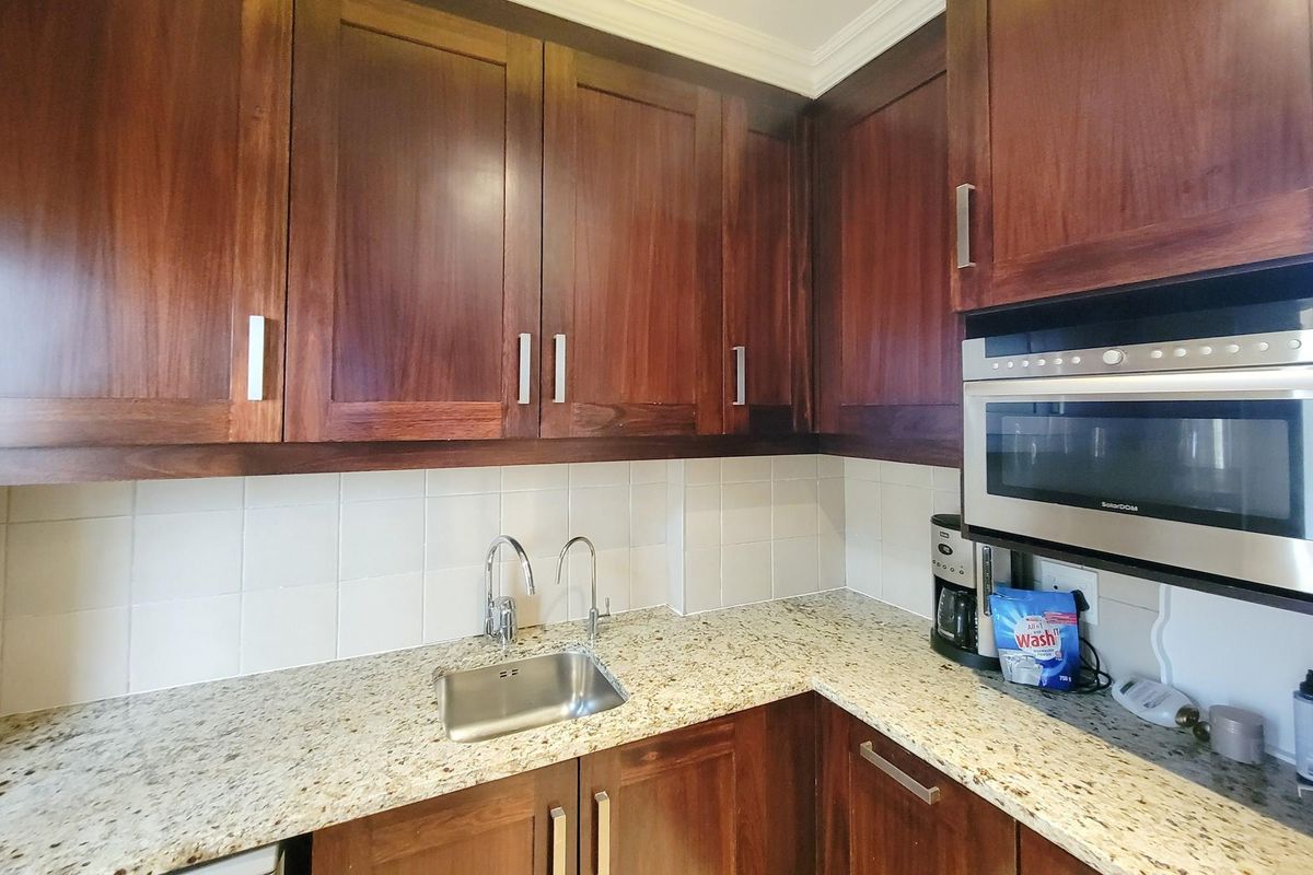 A functional kitchen area featuring dark wood cabinetry, granite countertops, a stainless steel sink, and a built-in microwave.